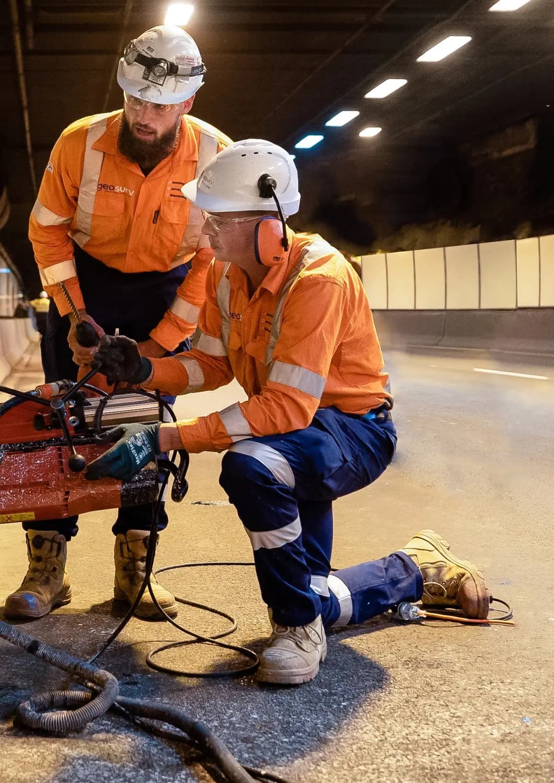 Two Geosurv technicians scanning a concrete slab with survey equipment inside a road tunnel