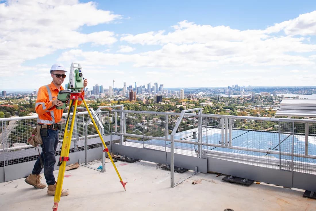 Geosurv surveyor operating a total station on a Sydney rooftop with the CBD skyline behind